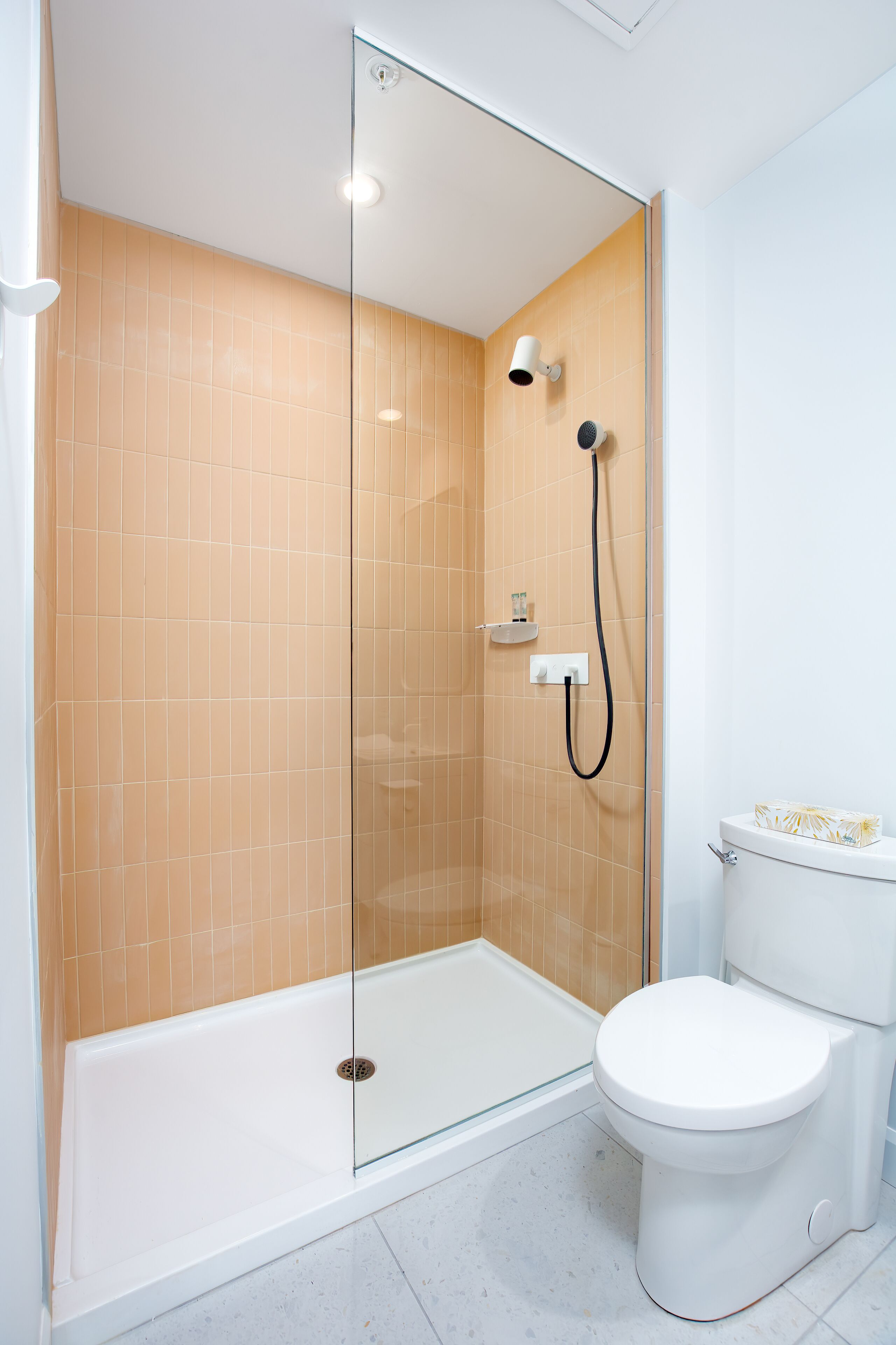 A modern bathroom with a glass-enclosed shower, a white toilet, and beige tiled walls.