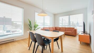 A modern living room with a dining table, chairs, a sofa, and a television.