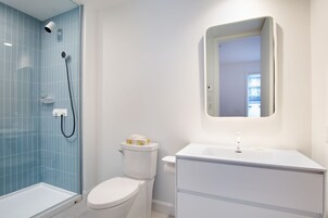 A bathroom with a glass-enclosed shower, a white toilet, and a white sink with a mirror above it.