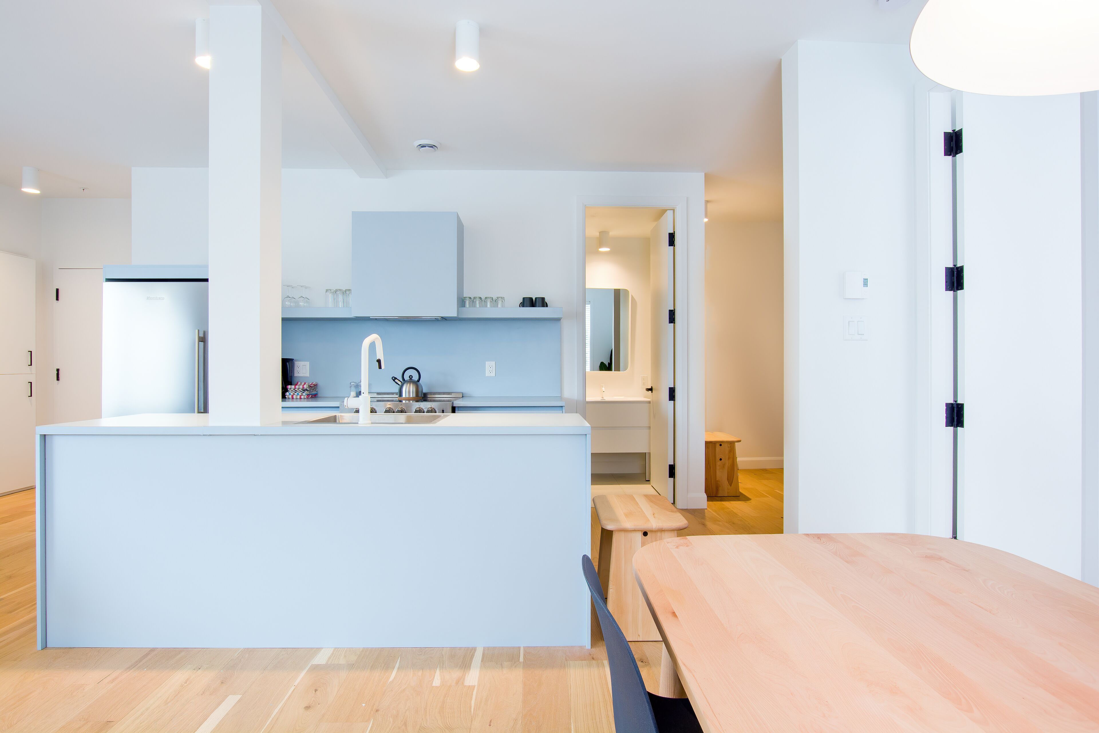 A modern kitchen with a central island, a dining area with a wooden table, and a visible door leading to another room.