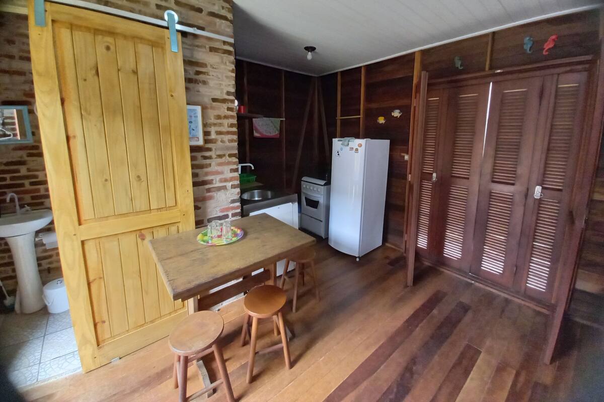 Eine kleine Küche mit Holzschränken, einem Spülbecken, einem Kühlschrank und einem Essbereich mit Hockern.
