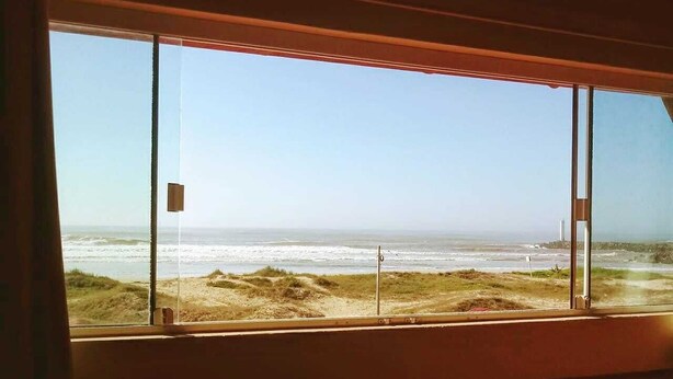 A room with a large window overlooking a beach with dunes and the ocean. - Pousada Moradas do Sol Nascente (Passo de Torres)