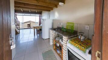 A compact kitchen with a built-in oven, a refrigerator, and a small dining area with a bench.