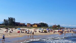 A beach with people, umbrellas, and buildings in the background. - Pousada Moradas do Sol Nascente (Passo de Torres)