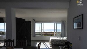 A room with a dining table, chairs, a bed, and a large window offering a view of the beach. - Pousada Moradas do Sol Nascente (Passo de Torres)
