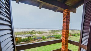 A balcony with a brick pillar, a view of the beach, and a small garden area. - Pousada Moradas do Sol Nascente (Passo de Torres)