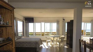 A bedroom with a bed, a dining area with a table and chairs, and a balcony with a view. - Pousada Moradas do Sol Nascente (Passo de Torres)