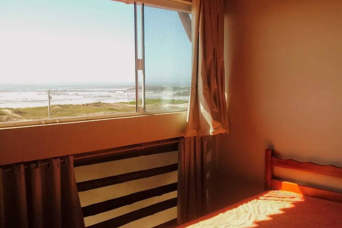 Ein Schlafzimmer mit Bett, einem Fenster mit Vorhängen und Blick auf den Strand.