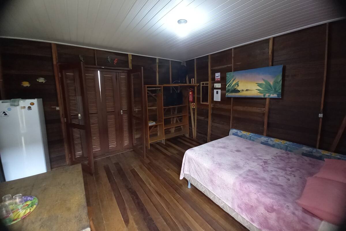 Ein Zimmer mit Bett, Kleiderschrank, Regalen und einem Kühlschrank.