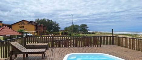 A wooden deck with lounge chairs and a swimming pool, overlooking a beach and a building labeled "Pousada Moradas do Sol Nascente".