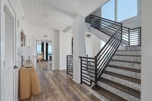A staircase with a geometric patterned railing, a wooden floor, and a white ceiling. - Oceanfront 8/4 | Industrial Chic | Large Groups (St. Augustine)