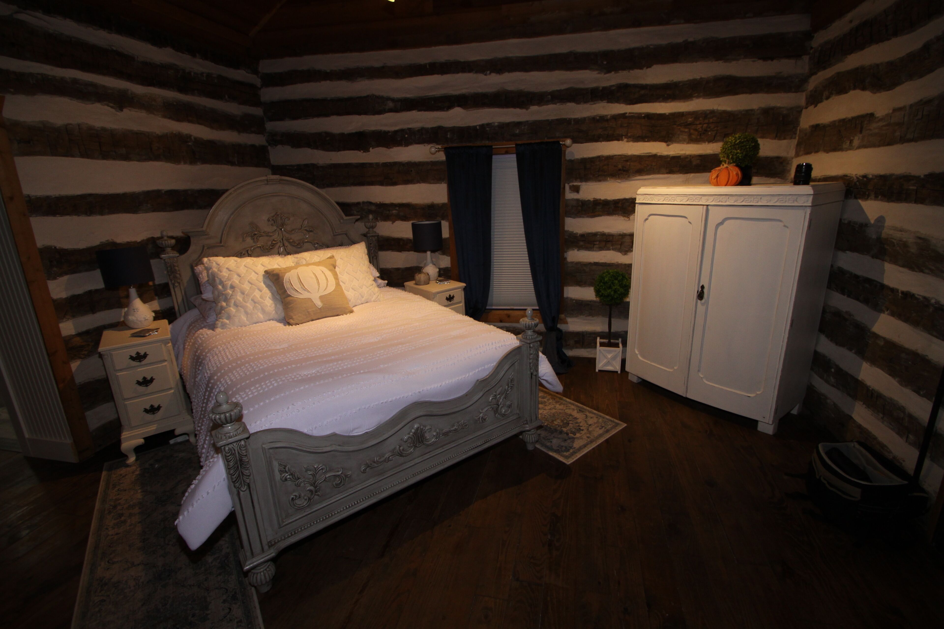 Un dormitorio con una cama grande, una mesita de noche, un aparador y una pequeña planta.