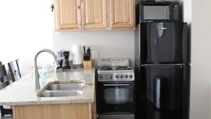 A kitchen with wooden cabinets, a stainless steel sink, a gas stove, a black refrigerator, and a microwave. - Jack's on the Bay, 2 Bedroom/2 Bath Lake Front (Denton Township)