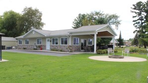 A two-story building with a covered patio area, a stone foundation, and a well-maintained lawn. - Jack's on the Bay, 2 Bedroom/2 Bath Lake Front (Denton Township)
