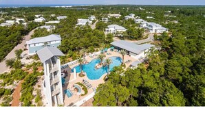 Eine Vogelperspektive zeigt ein Resort mit mehreren Gebäuden, einem zentralen Schwimmbecken und umgebender Bepflanzung.