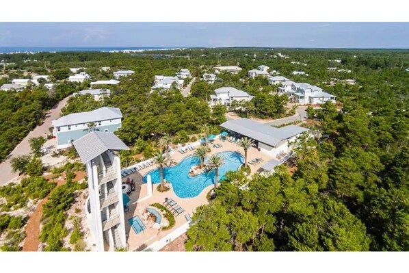 An aerial view of a resort with multiple buildings, a central swimming pool, and surrounding greenery.