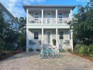 Une maison à deux étages avec un porche à l’avant, un vélo garé devant et un jardin bien entretenu.