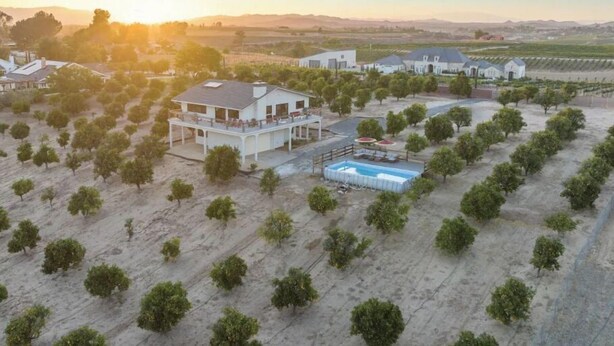 Una casa grande con piscina, rodeada por un viñedo, bajo un cielo despejado.