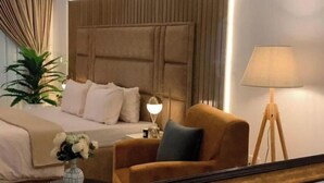 A hotel room with a large bed, a bedside table with a lamp, a chair, and a potted plant. - Ice Apartel Lekki phase 1 (Lagos)
