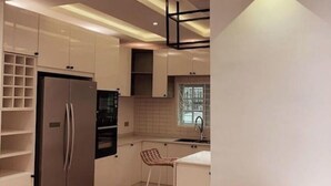 A modern kitchen with white cabinets, a stainless steel refrigerator, a built-in oven, and a bar stool. - Ice Apartel Lekki phase 1 (Lagos)