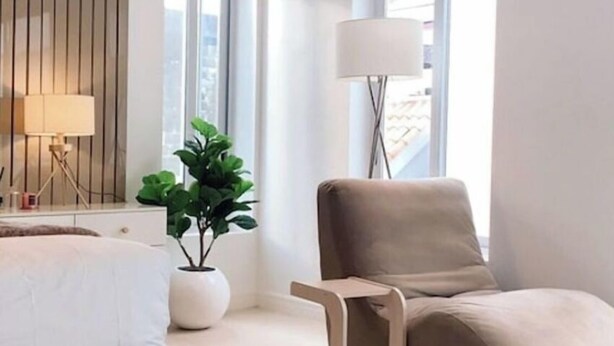 A modern hotel room with a bed, a chair, a floor lamp, a potted plant, and a window with a view of the city. - Ice Apartel Lekki phase 1 (Lagos)