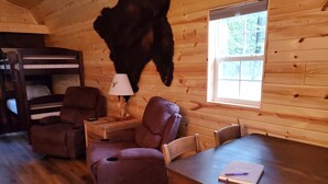 L’intérieur chaleureux d’un chalet avec un plancher en bois, une table à manger, deux fauteuils en cuir, une lampe et une peau d’animal empaillée accrochée au mur.