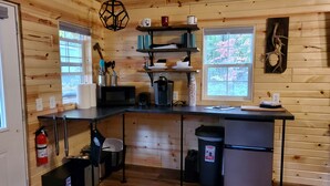 Une cuisine compacte aux murs en bois, dotée d’un îlot central et d’une fenêtre donnant sur un paysage verdoyant.
