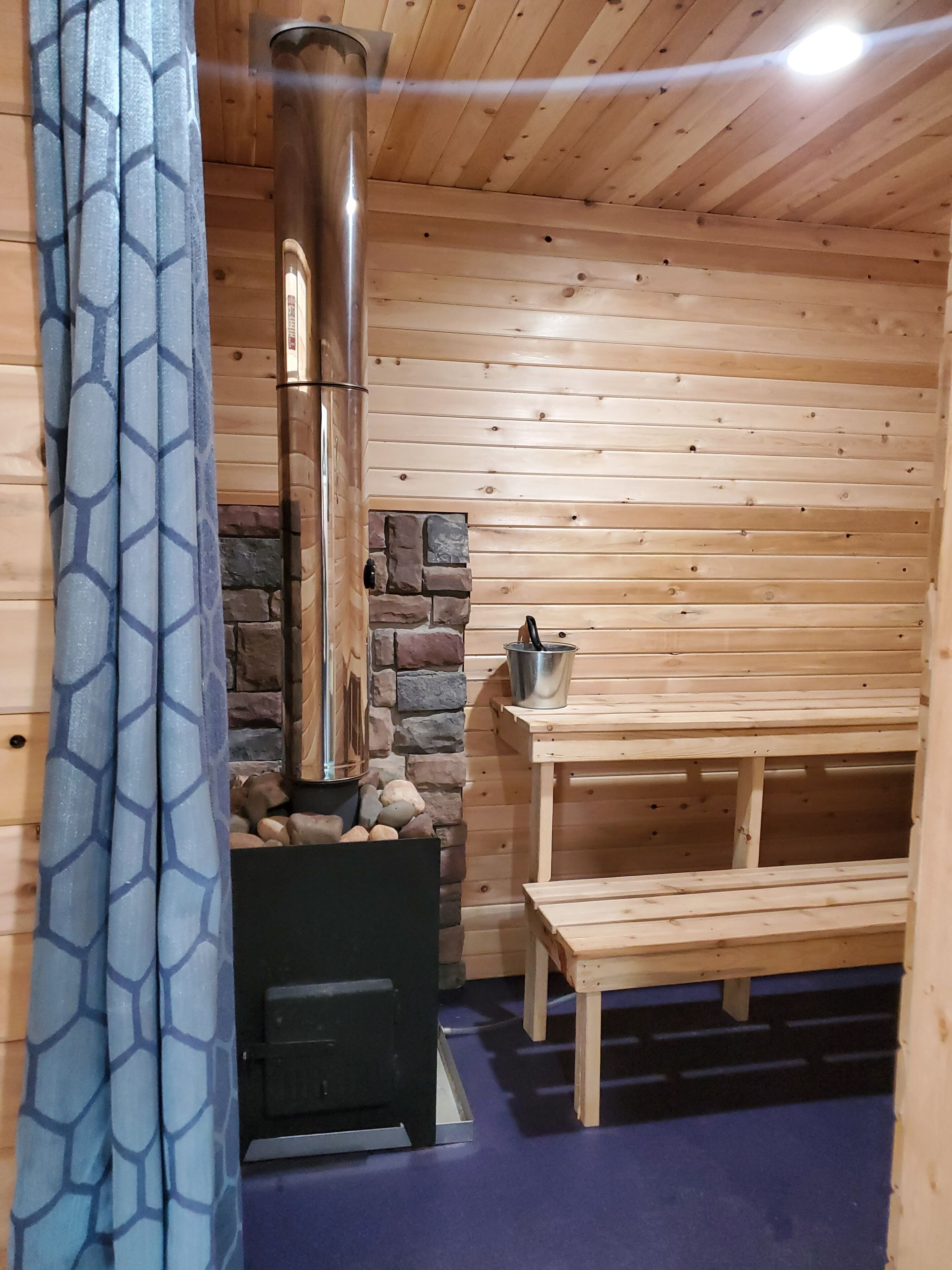 A wooden cabin interior with a stone fireplace, a bench, and a table.