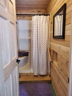 Une salle de bain rustique, avec des murs en bois, comprenant une douche, un porte-serviettes et un miroir.