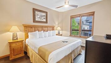 A bedroom with a large bed, wooden headboard, two bedside lamps, a ceiling fan, a window with a view, and a desk.