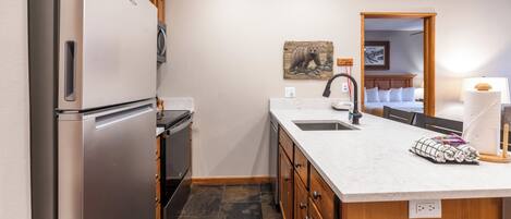 A modern kitchen with a stainless steel refrigerator, wooden cabinets, a marble countertop, and a sink.