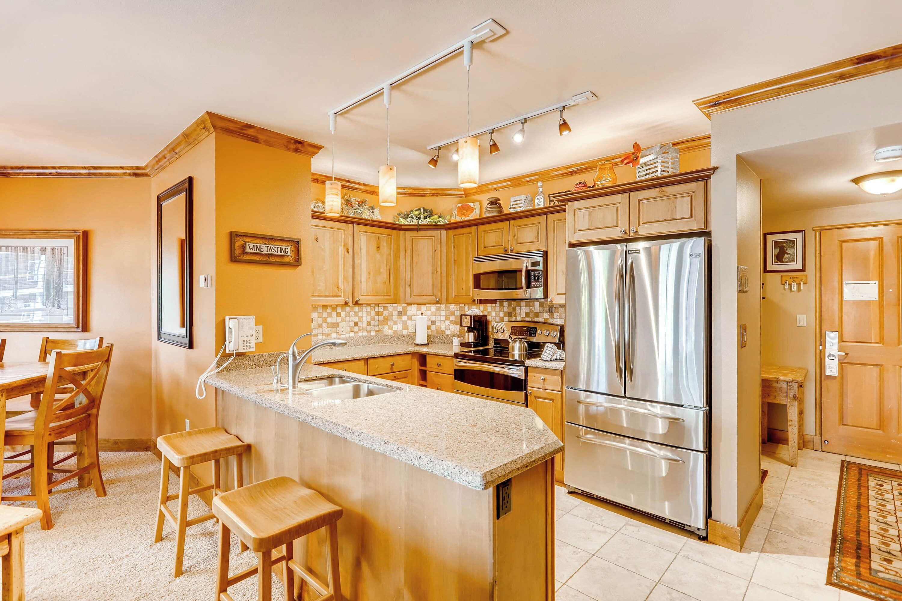 A kitchen with wooden cabinets, stainless steel appliances, a granite countertop, and a bar area with stools.