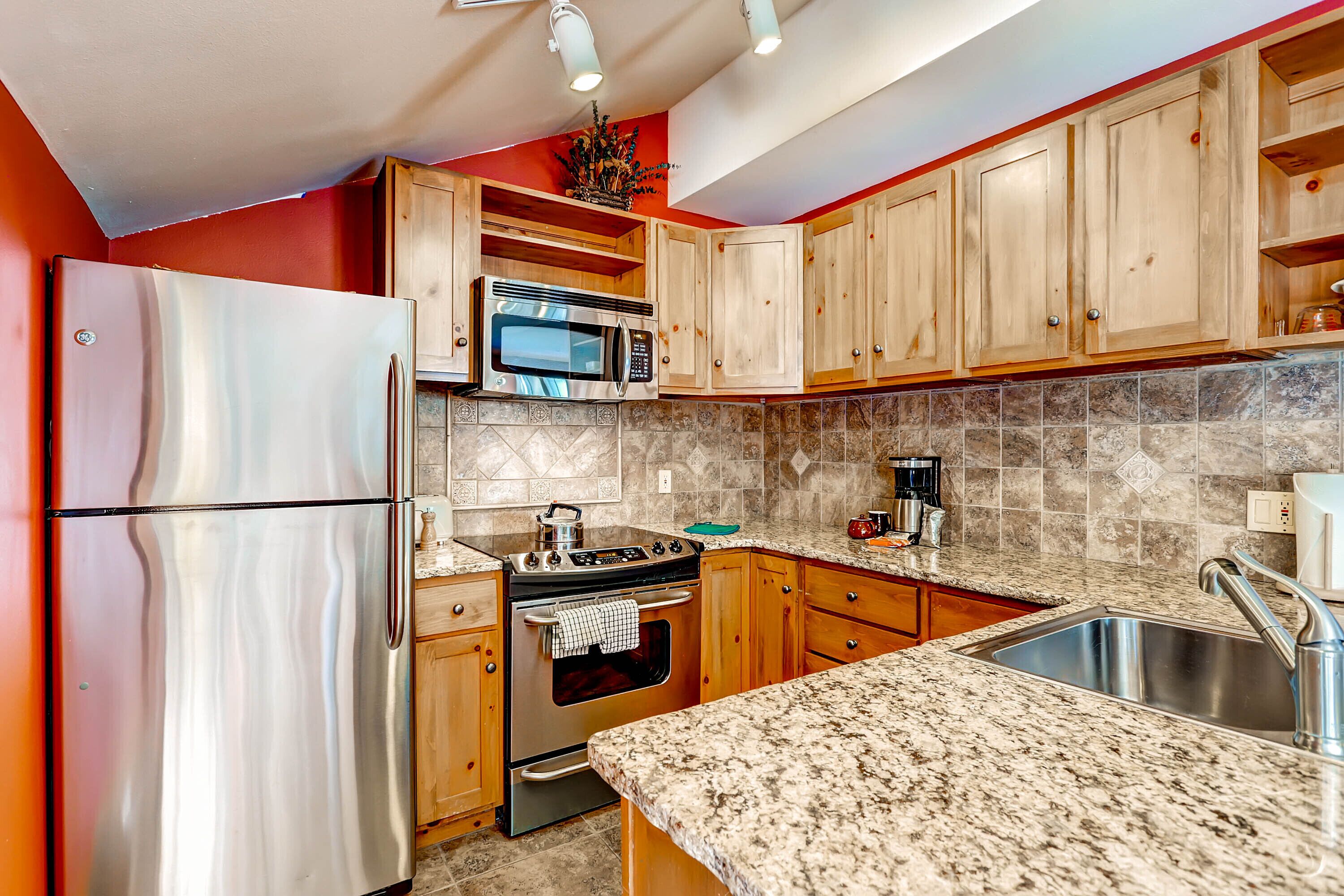 A kitchen with wooden cabinets, a stainless steel refrigerator, a microwave, an oven, and a granite countertop.