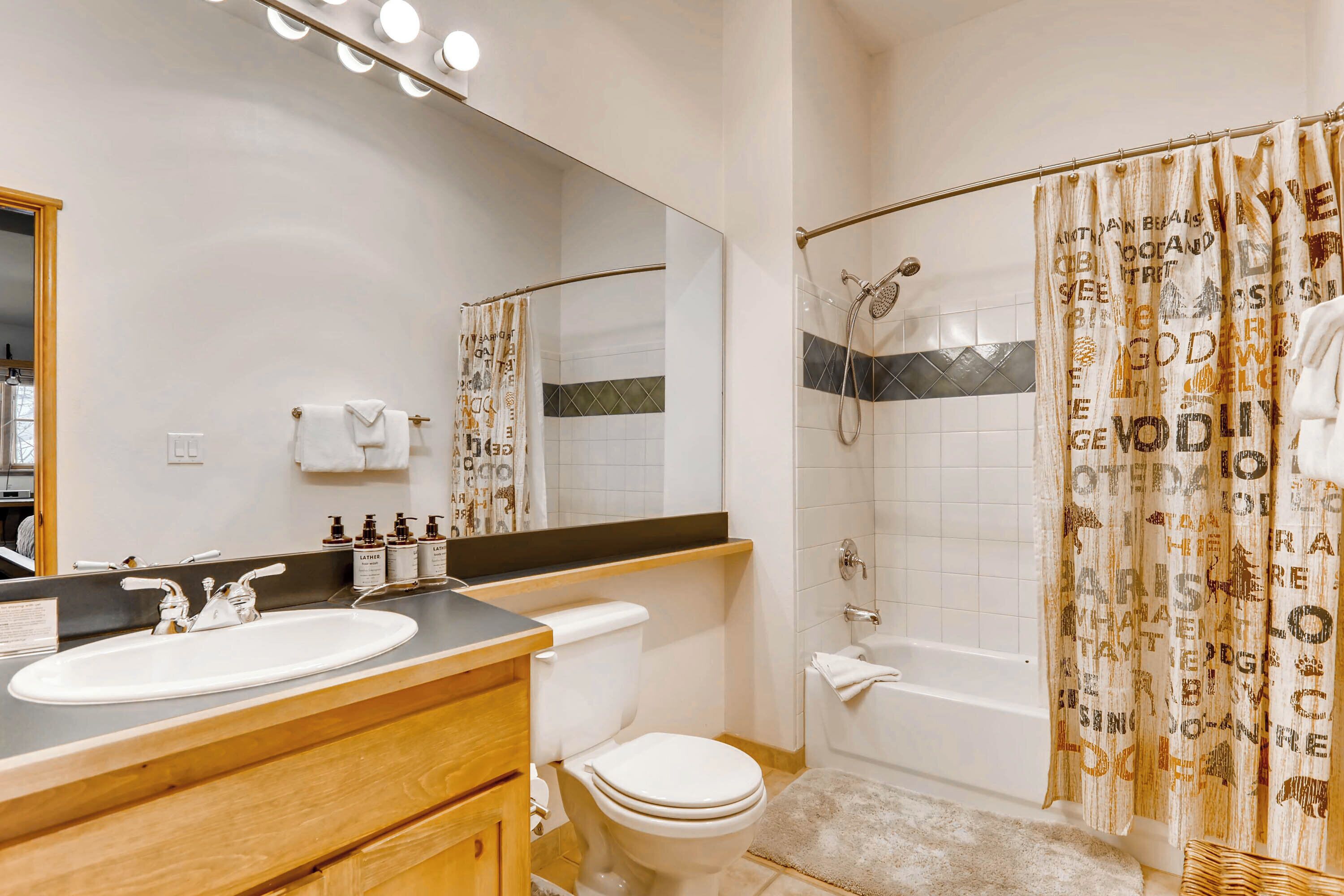 Un baño con lavamanos blanco, espejo, inodoro y cortina de ducha con texto.