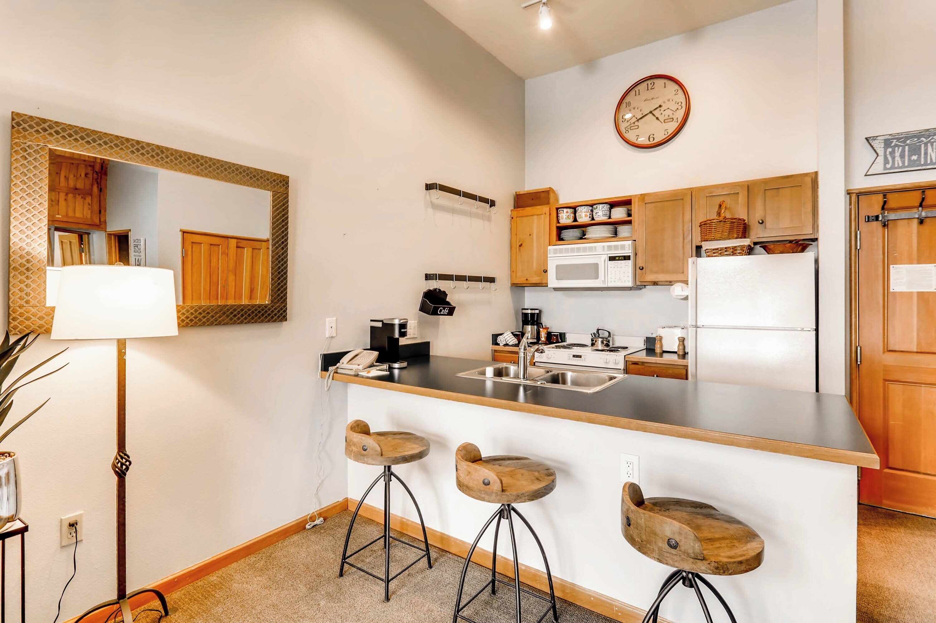 A compact kitchen with a central island, wooden bar stools, a microwave, and a refrigerator.