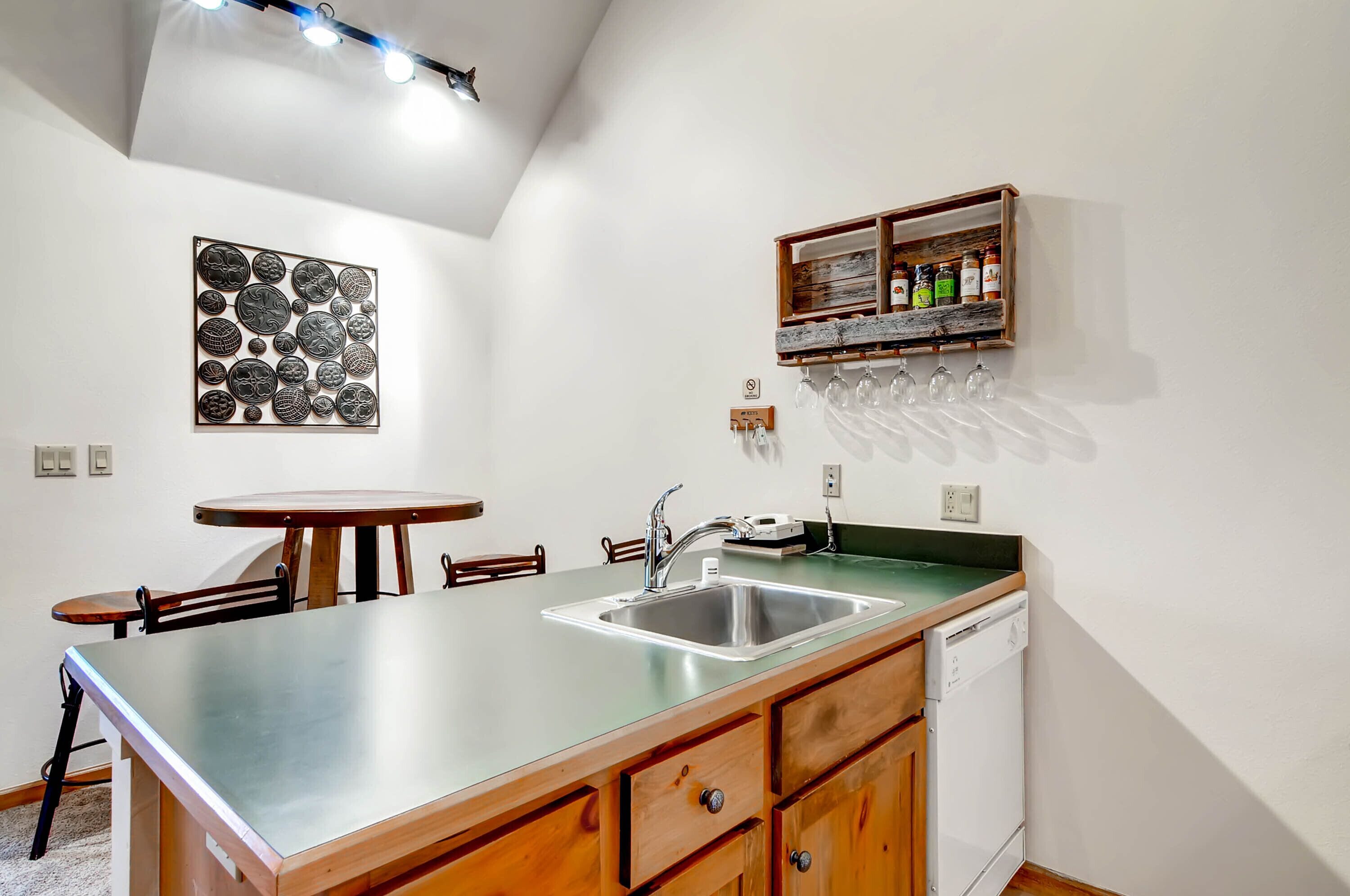 Una cocina compacta con un lavamanos, armarios de madera, una pequeña mesa de comedor y una estantería para vinos en la pared.