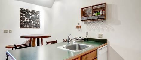 Una cocina compacta con un lavamanos, armarios de madera, una pequeña mesa de comedor y una estantería para vinos en la pared.
