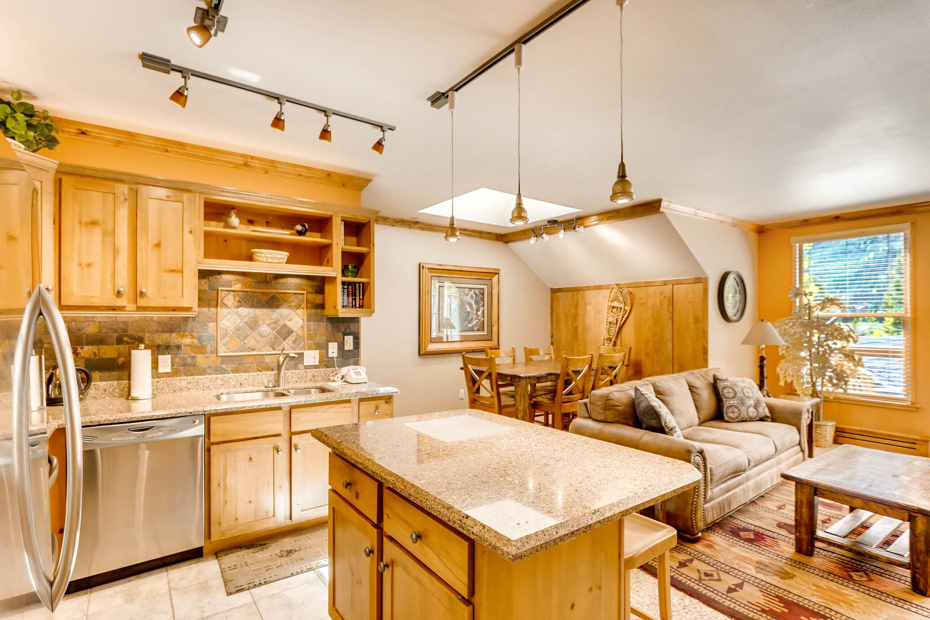 Una cocina amplia con armarios de madera, encimera de granito y comedor con sofá y mesa.