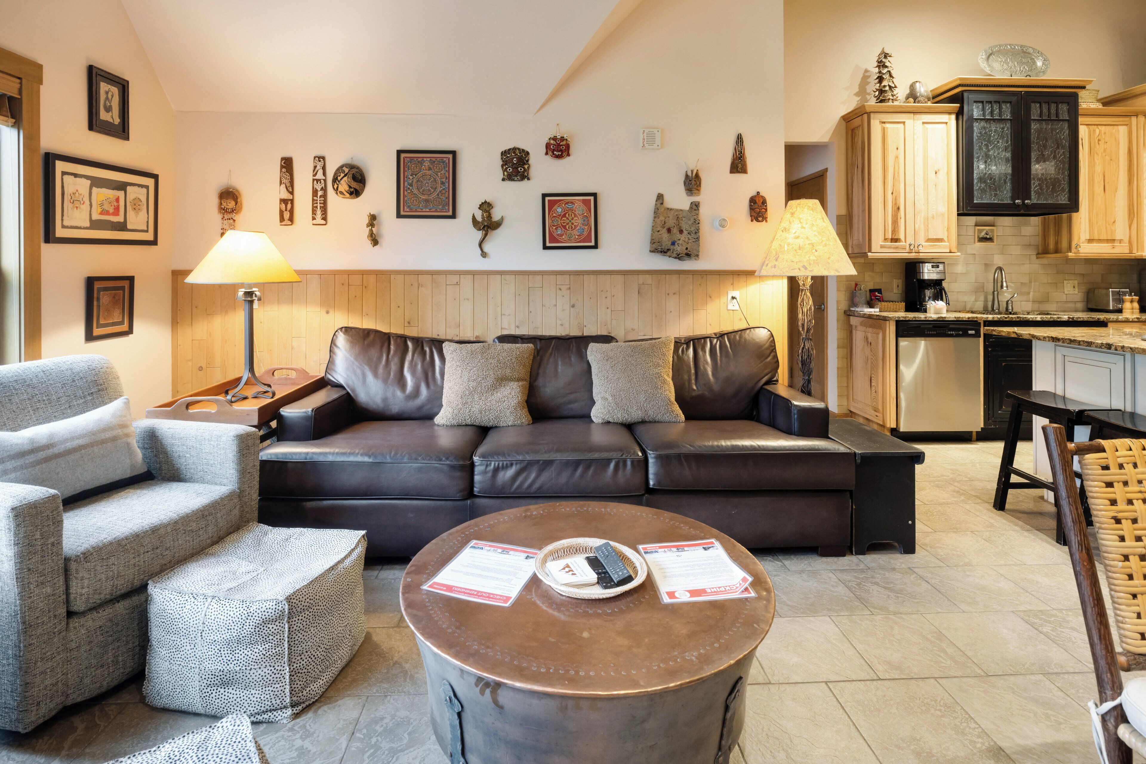A living room with a brown leather sofa, grey armchairs, and a round coffee table with papers.
