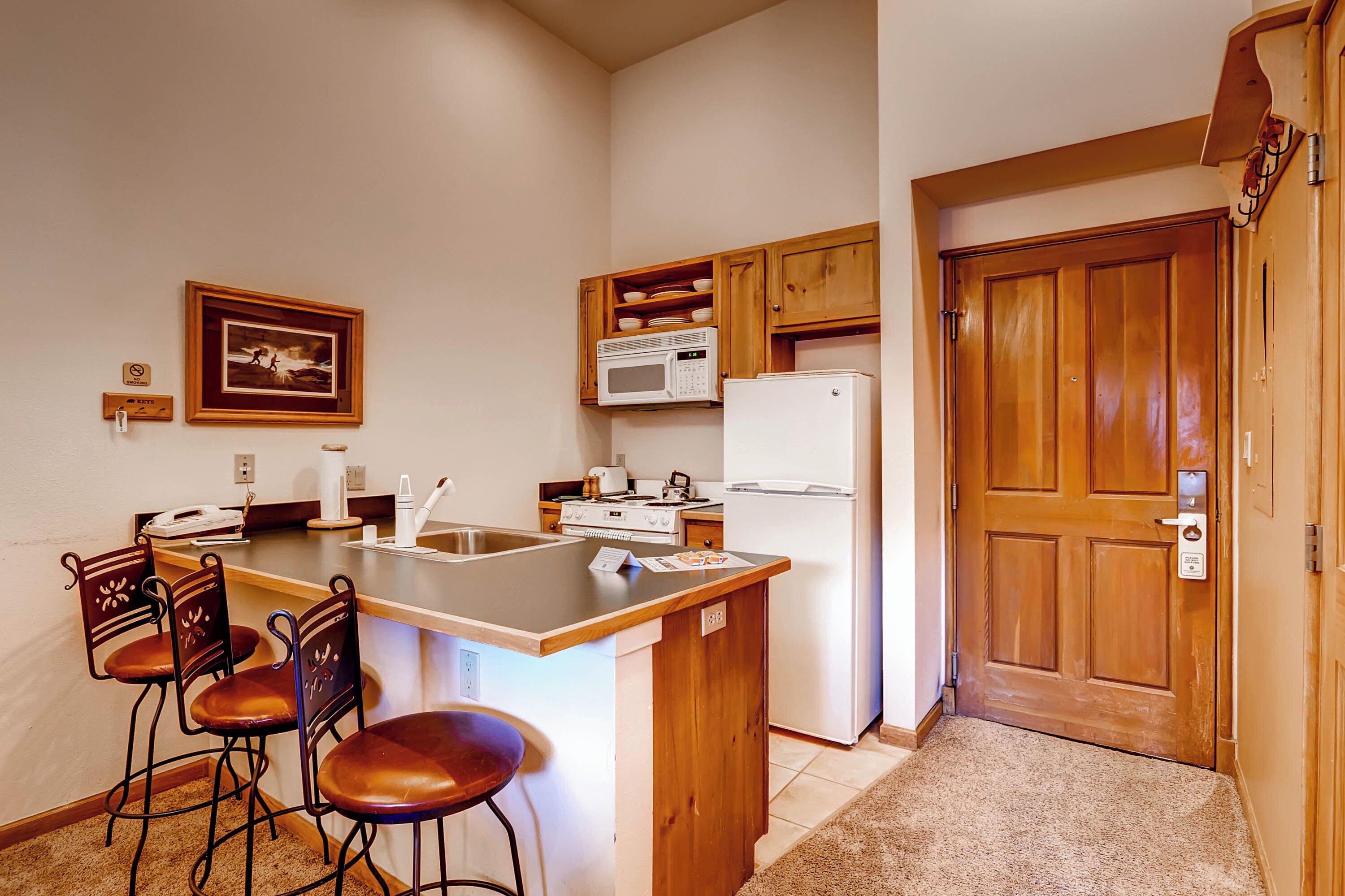 Cocina compacta con una isla central, taburetes de bar, microondas, refrigerador y armarios de madera.