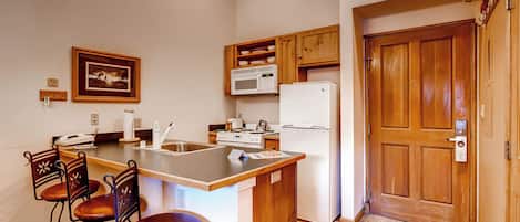 Cocina compacta con una isla central, taburetes de bar, microondas, refrigerador y armarios de madera.
