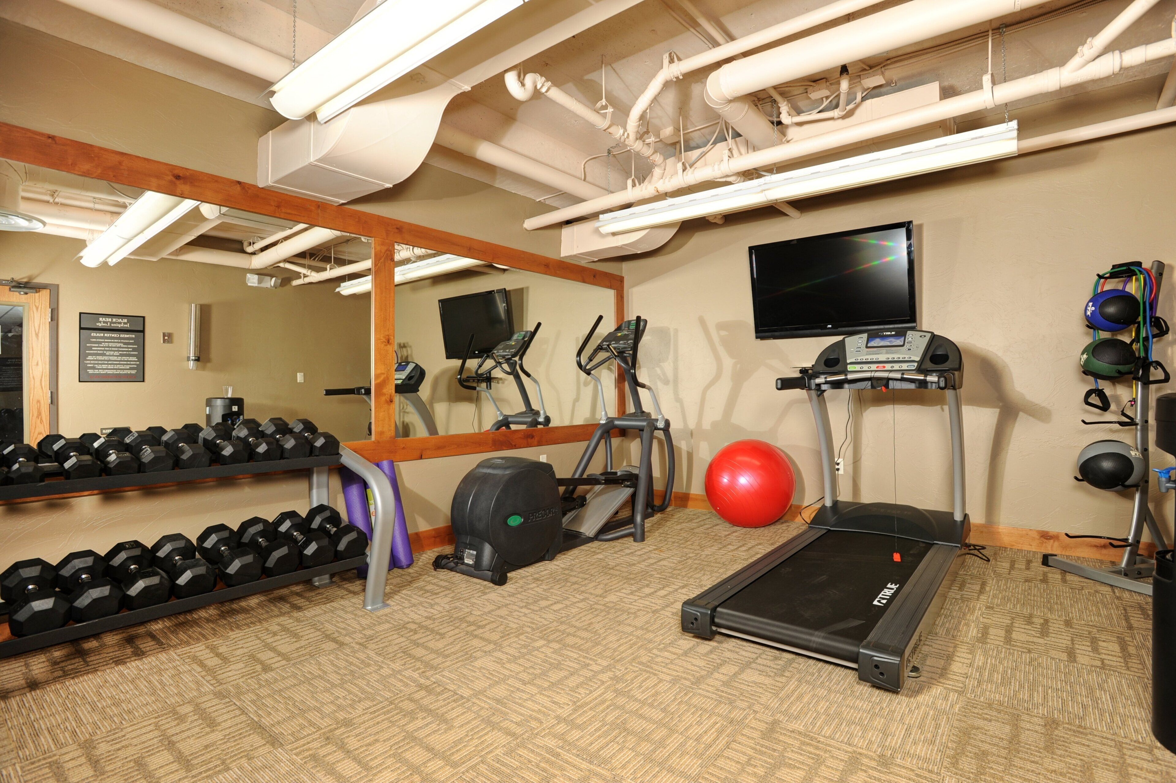A gym with exercise equipment, a treadmill, a mirrored wall, and a TV.