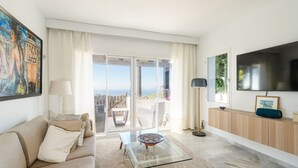 Una sala de estar moderna con una mesa de centro de vidrio, un sofá color beige y un televisor grande en la pared.