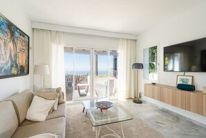 Un salon moderne avec un canapé, une table basse en verre, un téléviseur et une vue sur l’extérieur.
