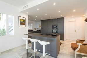 A modern kitchen with a central island, bar stools, and a dining area with wicker chairs.