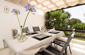 Un espace de restauration en plein air avec une table dressée pour deux personnes, un banc et une vue sur la verdure.