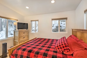 Une chambre à coucher avec un lit, une commode, un téléviseur et des fenêtres donnant sur un paysage enneigé.