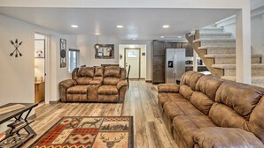 A spacious living room with two brown leather sofas, a wooden coffee table, and a patterned rug. A staircase leads to a kitchen area with modern appliances. - Cozy two bedroom cabin 10 min from Red Rocks 25 min from Denver  (Morrison)