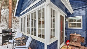 A covered porch with a grill, chairs, and a wood-burning stove. - Cozy two bedroom cabin 10 min from Red Rocks 25 min from Denver  (Morrison)