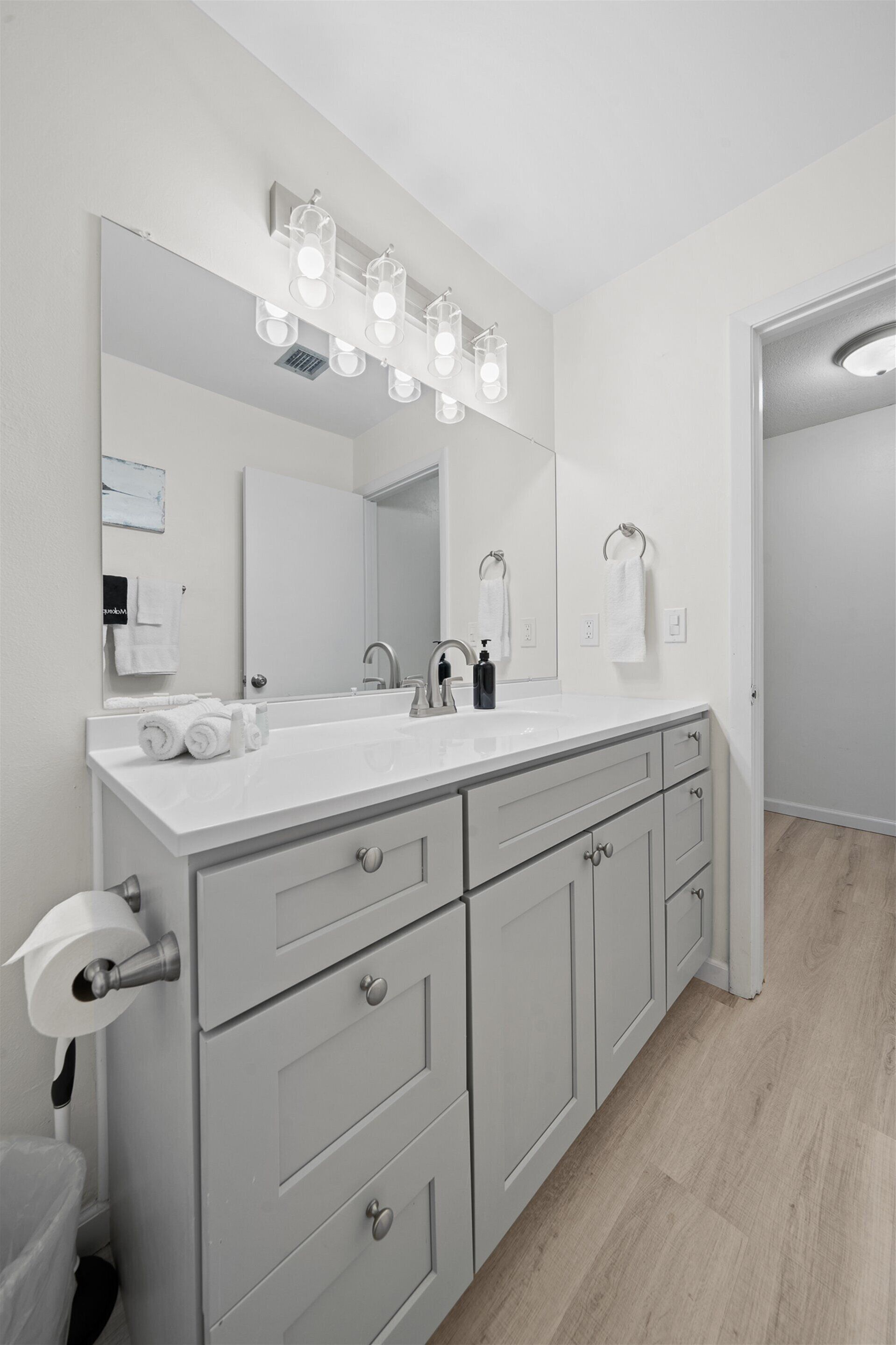 A modern bathroom with a large mirror, white sink, and grey cabinets.